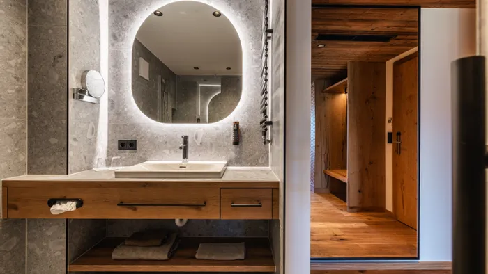Bagno moderno con specchio rotondo retroilluminato, pareti in pietra e mobile in legno accanto al corridoio